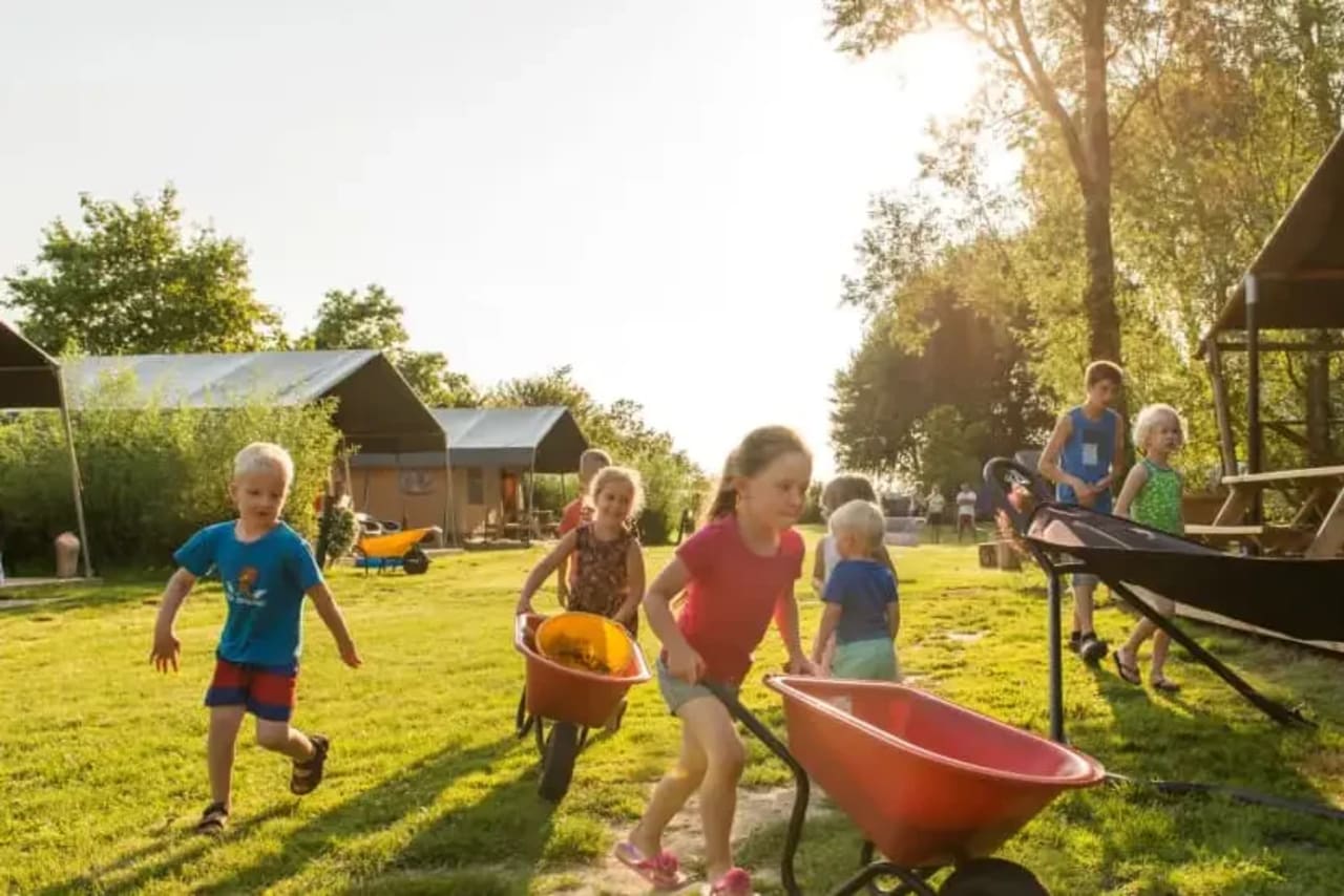 Kinder spielen auf dem Bauernhof mit Schubkarren während eines FarmCamps Urlaubs