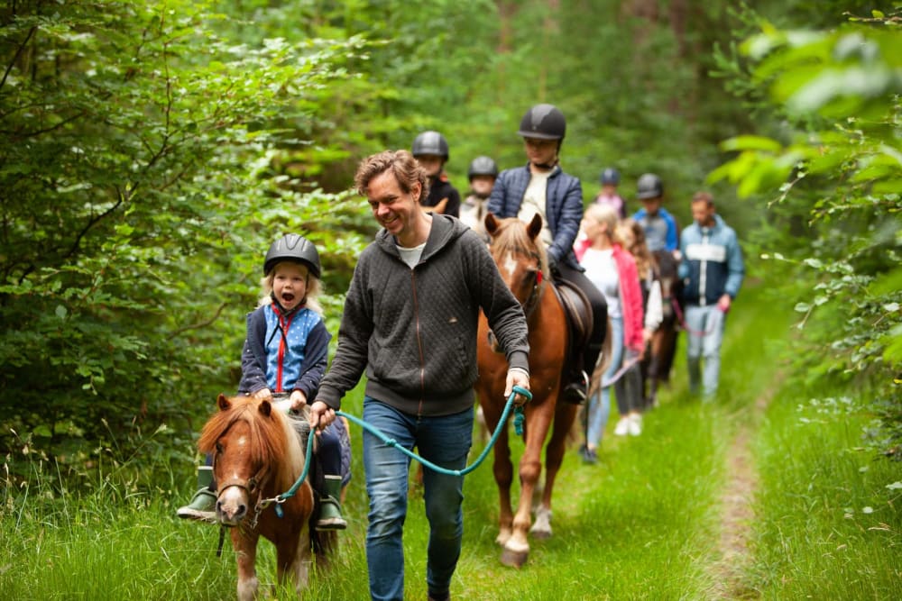 Kinderen maken een ponyrit door het bos tijdens een boerderijvakantie in Drenthe