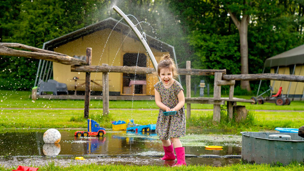 Girl playing with water and toys in front of a FarmCamps tent at De Geele Bosch