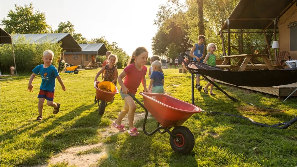 FarmCamps_Five_Star_kinderen_rennen_over_tentenveld_kruiwagen_meisje